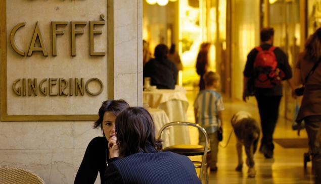 People chatting outside Caffè Gingerino in Bozano, with shoppers walking through the Lauben in the background.
