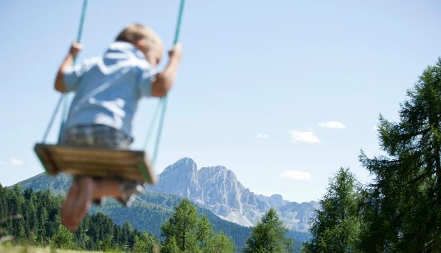 On the foreground, a little kid on a swing; on the background, the Dolomites.